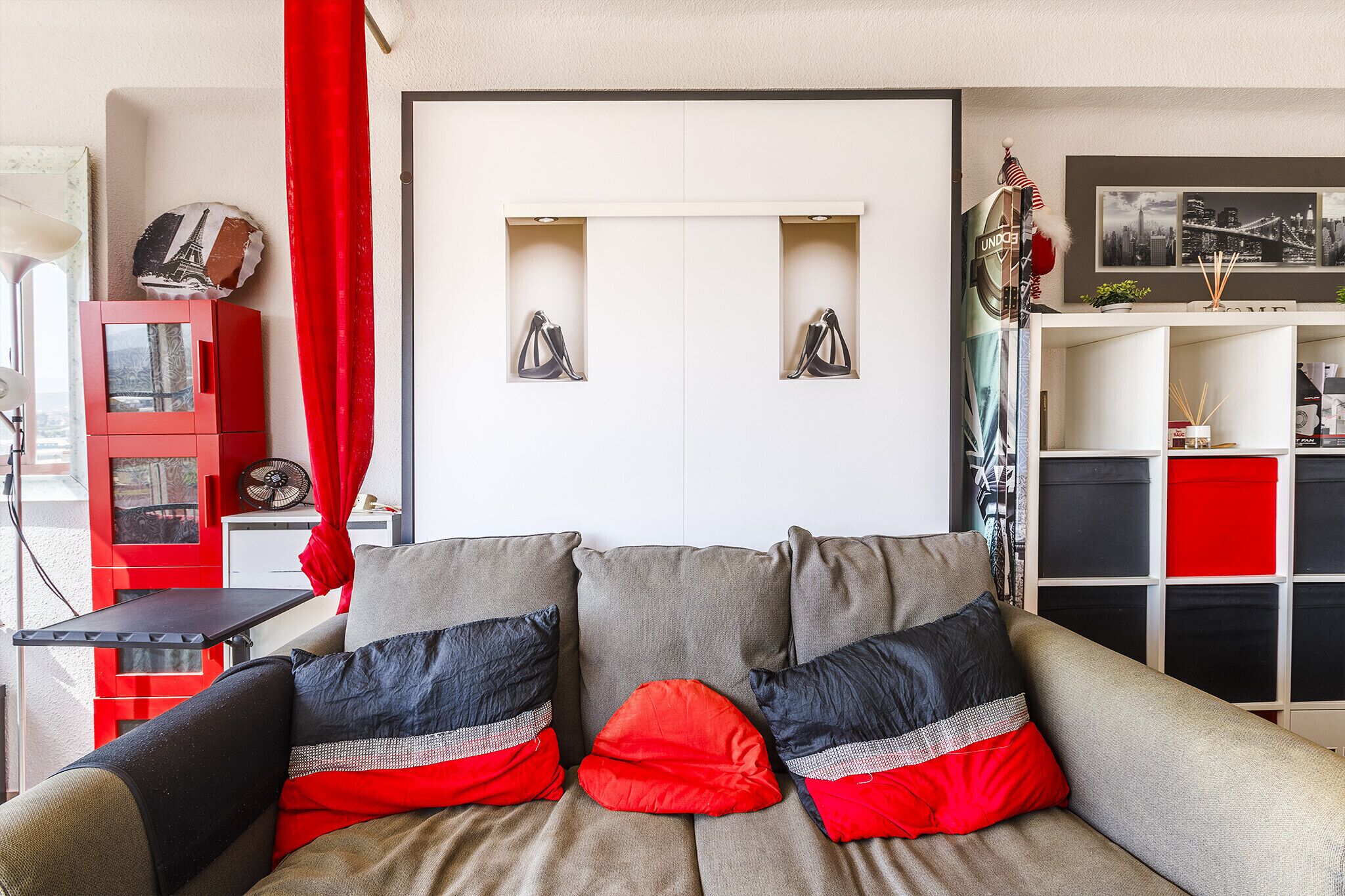A living room with a sofa, red curtains, a red cabinet, and a white wall with two picture frames.