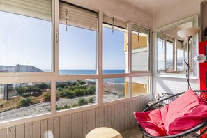 A room with large windows overlooking a beach and cityscape, a red chair, and a small table. - Algarrobo Beach 7, Algarrobo Costa (Algarrobo Costa)
