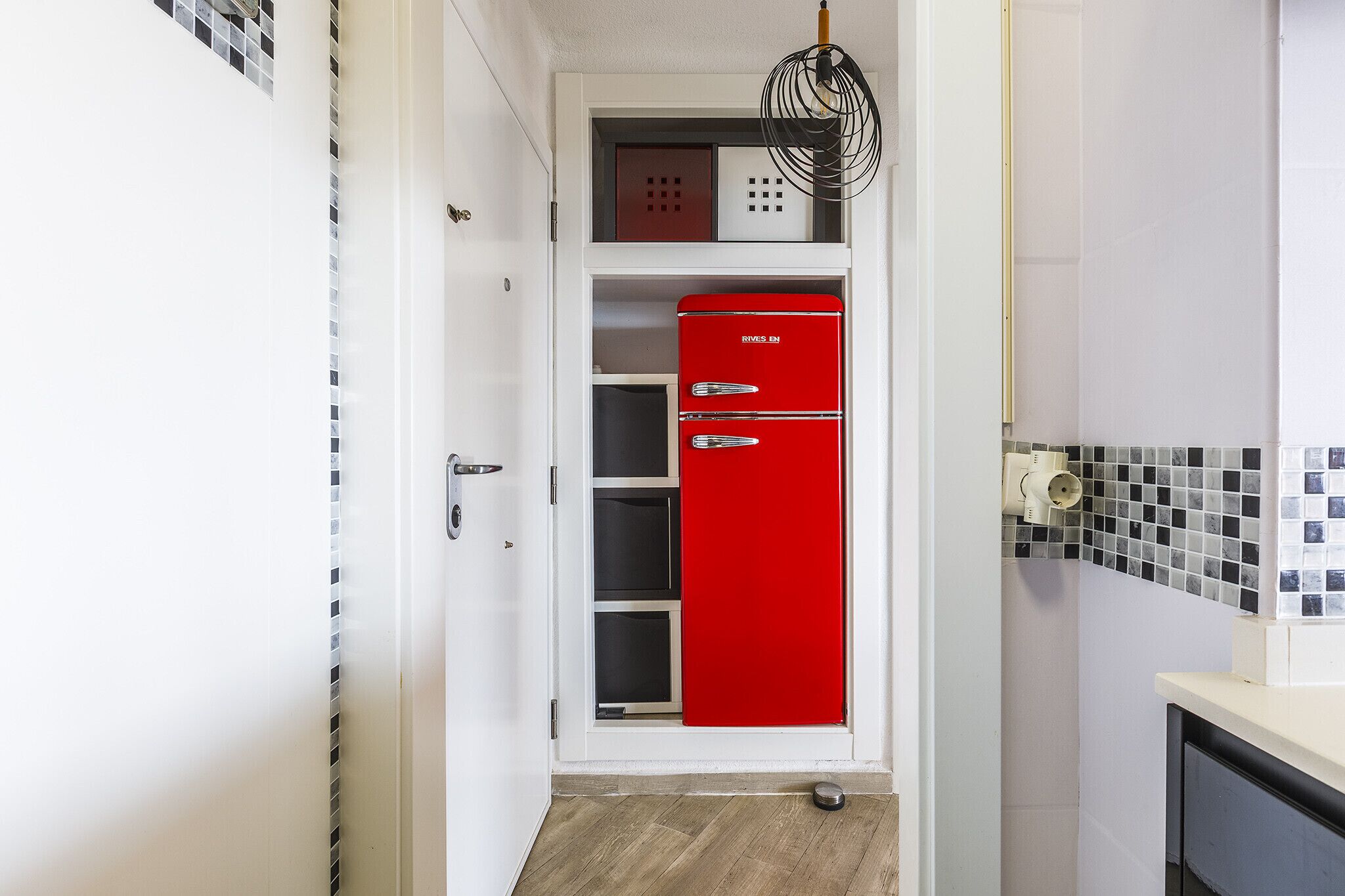 A narrow hallway with a red refrigerator, a white door, and a tiled backsplash.