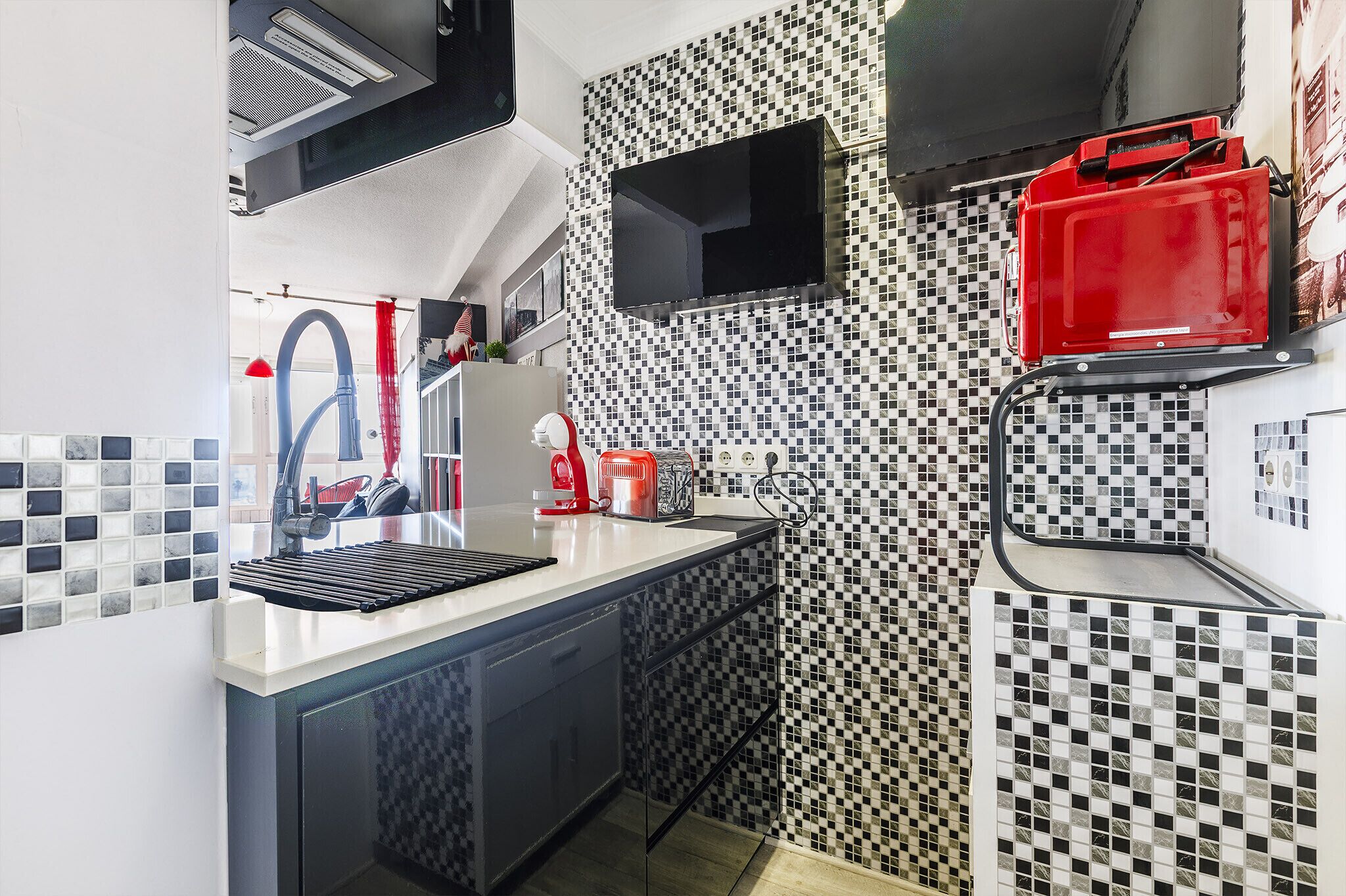 Uma cozinha compacta com pia, torradeira e um eletrodoméstico vermelho na bancada.