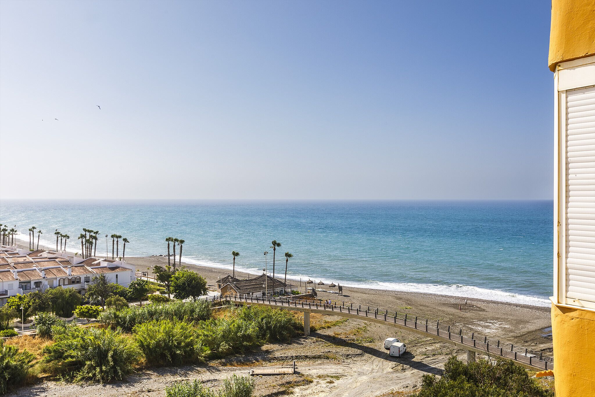 A coastal view with a beach, a fence, and buildings in the foreground.