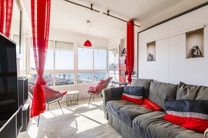 A living room with a sofa, red curtains, a TV, and a view of the city. - Algarrobo Beach 7, Algarrobo Costa (Algarrobo Costa)