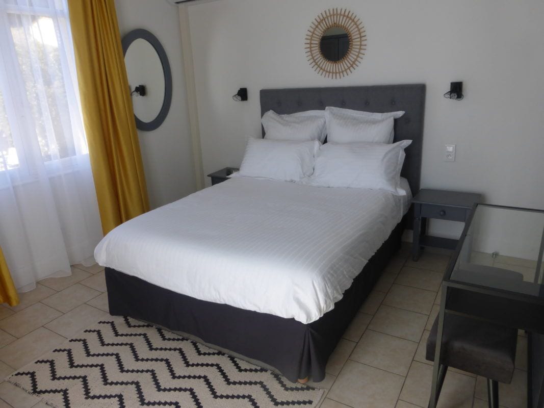 Un lit bien fait, avec du linge de lit blanc, dans une pièce au design moderne, comprenant un grand miroir rond fixé au mur et une petite table de chevet.