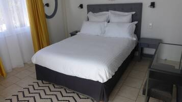 Un lit bien fait, avec du linge de lit blanc, dans une pièce au design moderne, comprenant un grand miroir rond fixé au mur et une petite table de chevet.