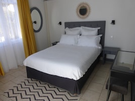 Una cama bien tendida con sábanas blancas en una habitación de diseño moderno, que incluye un espejo redondo en la pared y una pequeña mesita de noche.