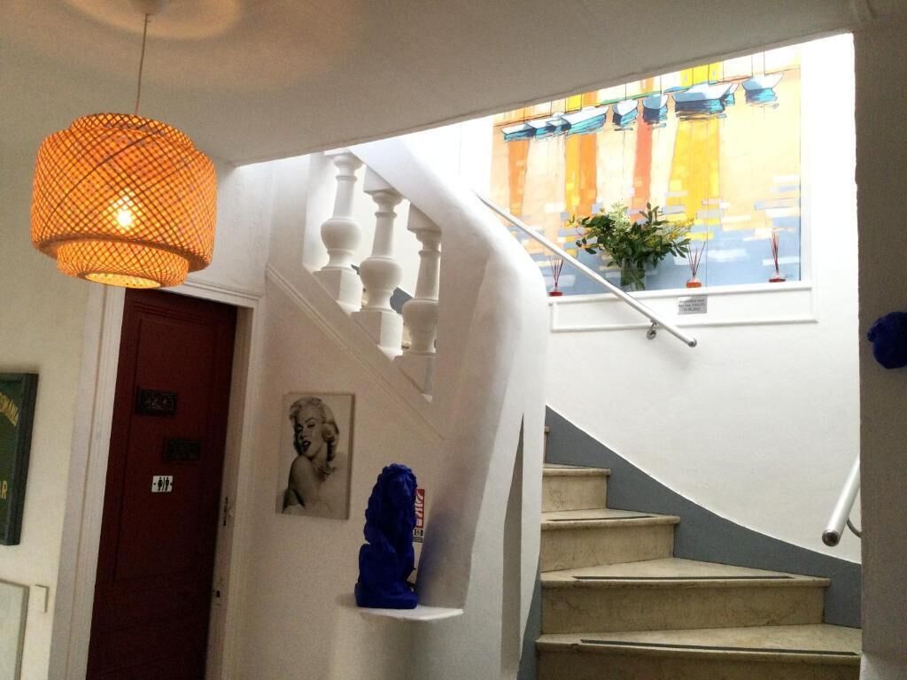 Eine Treppe mit weißer Brüstung, eine hängende orangefarbene Pendelleuchte und ein Fenster mit farbenfrohem Blick.