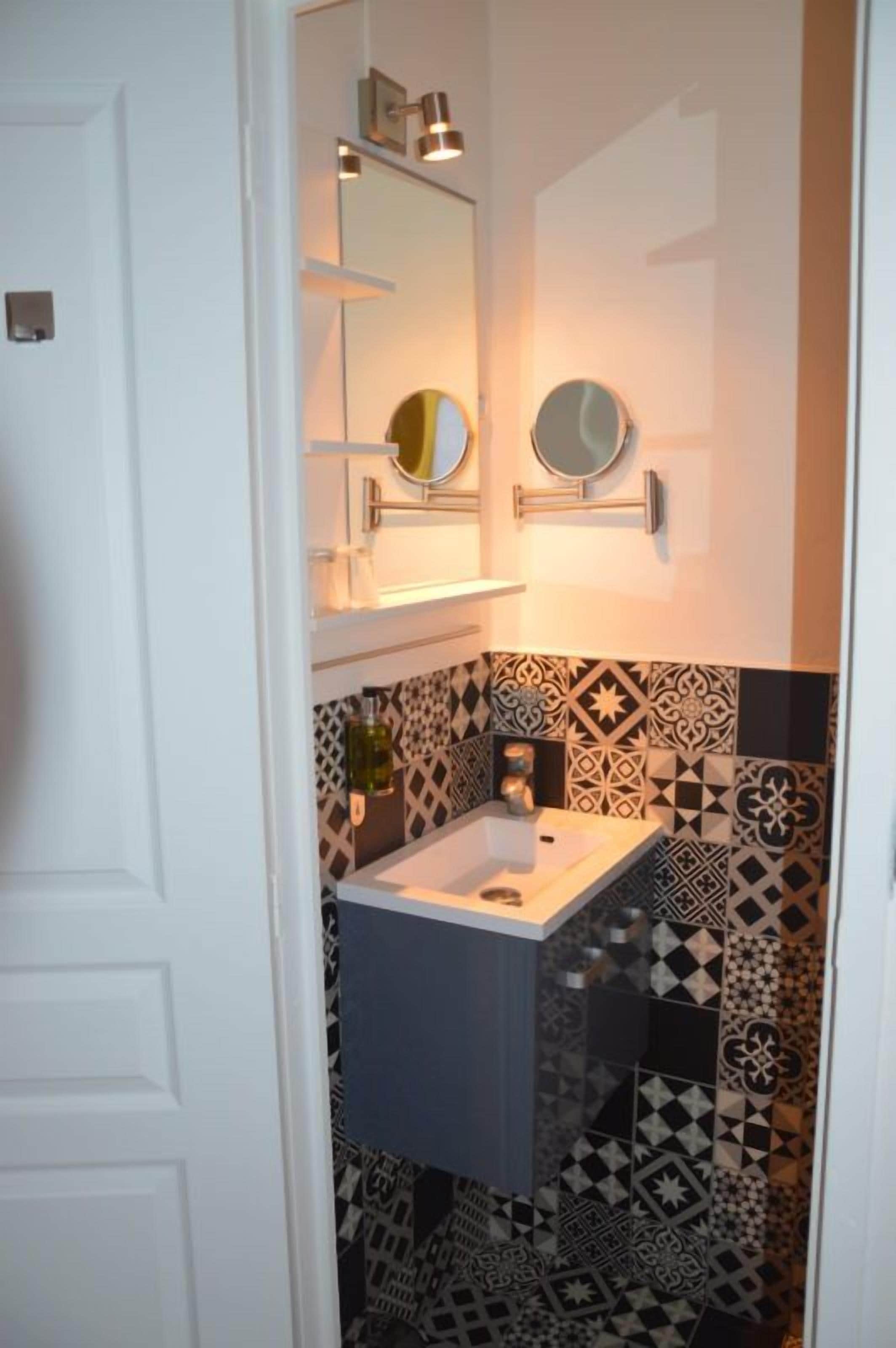 Un baño con una puerta blanca, un lavamanos con un espejo encima y azulejos decorativos en las paredes.
