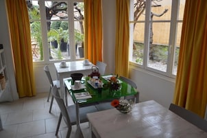 Un comedor con una mesa dispuesta para dos personas, una ventana con cortinas y vistas al jardín.