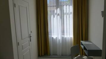 Une pièce avec une porte blanche, une fenêtre ornée de rideaux jaunes et un petit bureau avec une chaise.