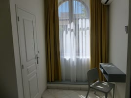 A room with a white door, a window with yellow curtains, and a small desk with a chair.