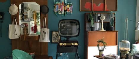 Una habitación con paredes verde azulado, un televisor antiguo, un armario de madera y una pequeña mesa con libros y un juguete.