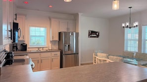 A modern kitchen with stainless steel appliances, a dining area with a glass table, and a chandelier. - Harmony: 3BR/2BA Cozy Retreat w/ Spa, Sun Deck & Boat Parking (Marathon)