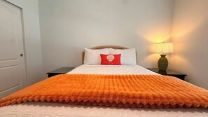 A bed with a white and orange blanket, a red pillow, and a lamp on a bedside table. - Harmony: 3BR/2BA Cozy Retreat w/ Spa, Sun Deck & Boat Parking (Marathon)