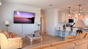 A modern living room with a flat-screen TV, leather sofas, a glass coffee table, and a kitchen with bar stools. - Harmony: 3BR/2BA Cozy Retreat w/ Spa, Sun Deck & Boat Parking (Marathon)
