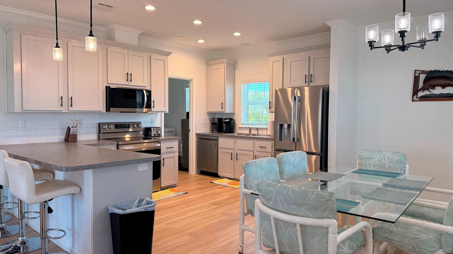 A modern kitchen with white cabinetry, stainless steel appliances, and a glass dining table with matching chairs.