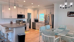 A modern kitchen with white cabinetry, stainless steel appliances, and a glass dining table with matching chairs. - Harmony: 3BR/2BA Cozy Retreat w/ Spa, Sun Deck & Boat Parking (Marathon)
