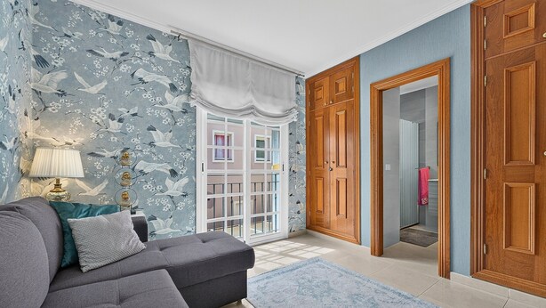 Een kamer met een grijze bank, blauw behang met patroon en een houten garderobe.