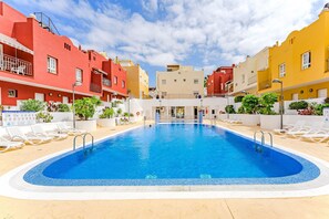 Piscina rodeada por edifícios coloridos, com espreguiçadeiras e um céu claro.