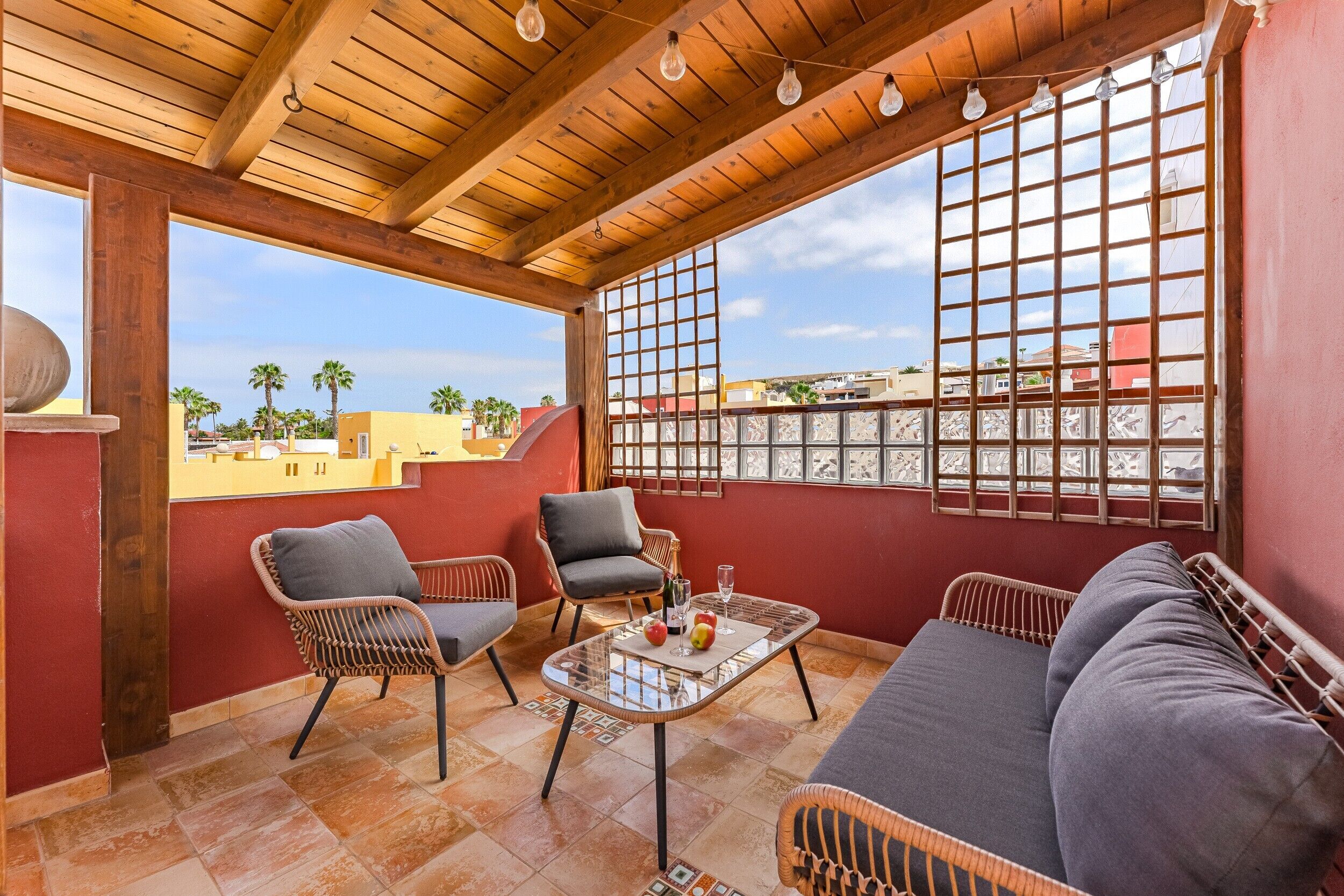 Un balcone con mobili in vimini, un tavolo in vetro e vista sulla città.