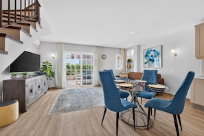 A modern living room with a dining area, a staircase, and a view of the outdoors.