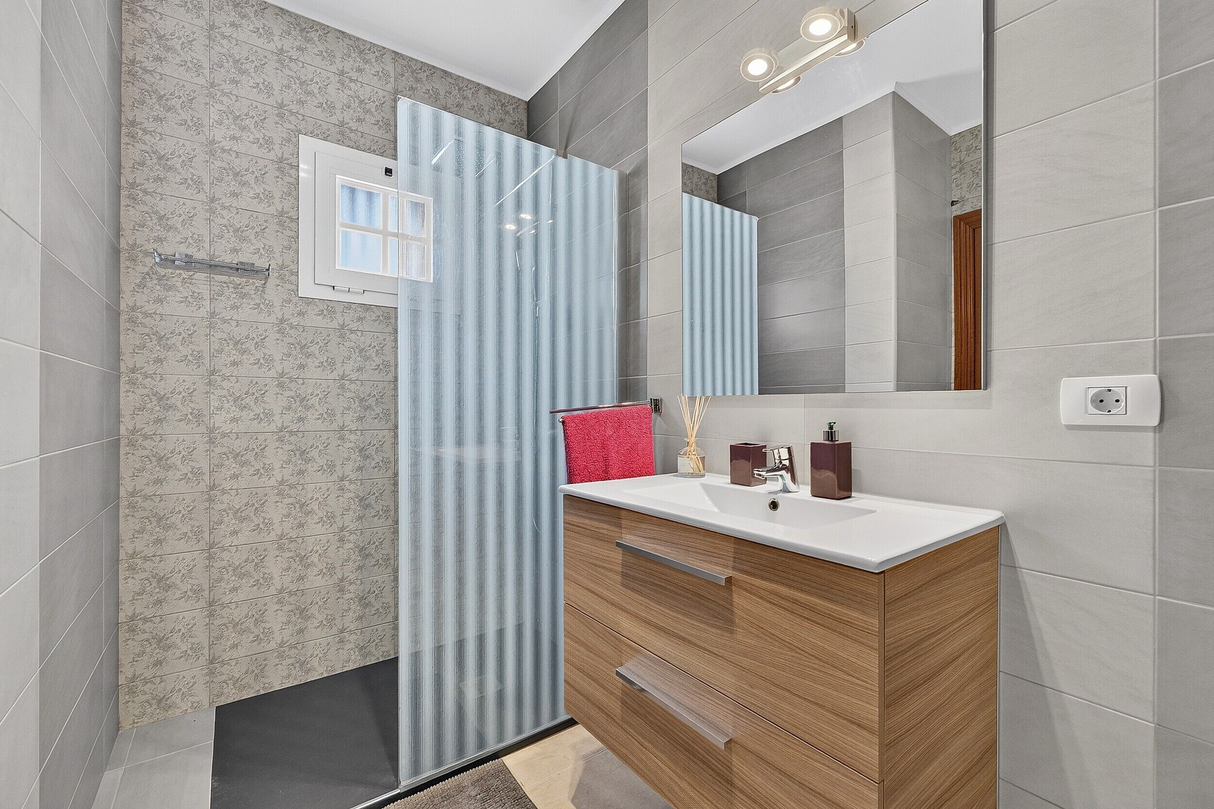 Un baño moderno con tocador de madera, un espejo grande y una ducha con puerta de cristal.
