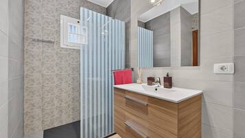 Un baño moderno con tocador de madera, un espejo grande y una ducha con puerta de cristal.