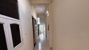 A corridor with doors on the left, a fire extinguisher on the right, and a window at the end. - Ollection O Sector 95B Gurgaon (Gurugram)