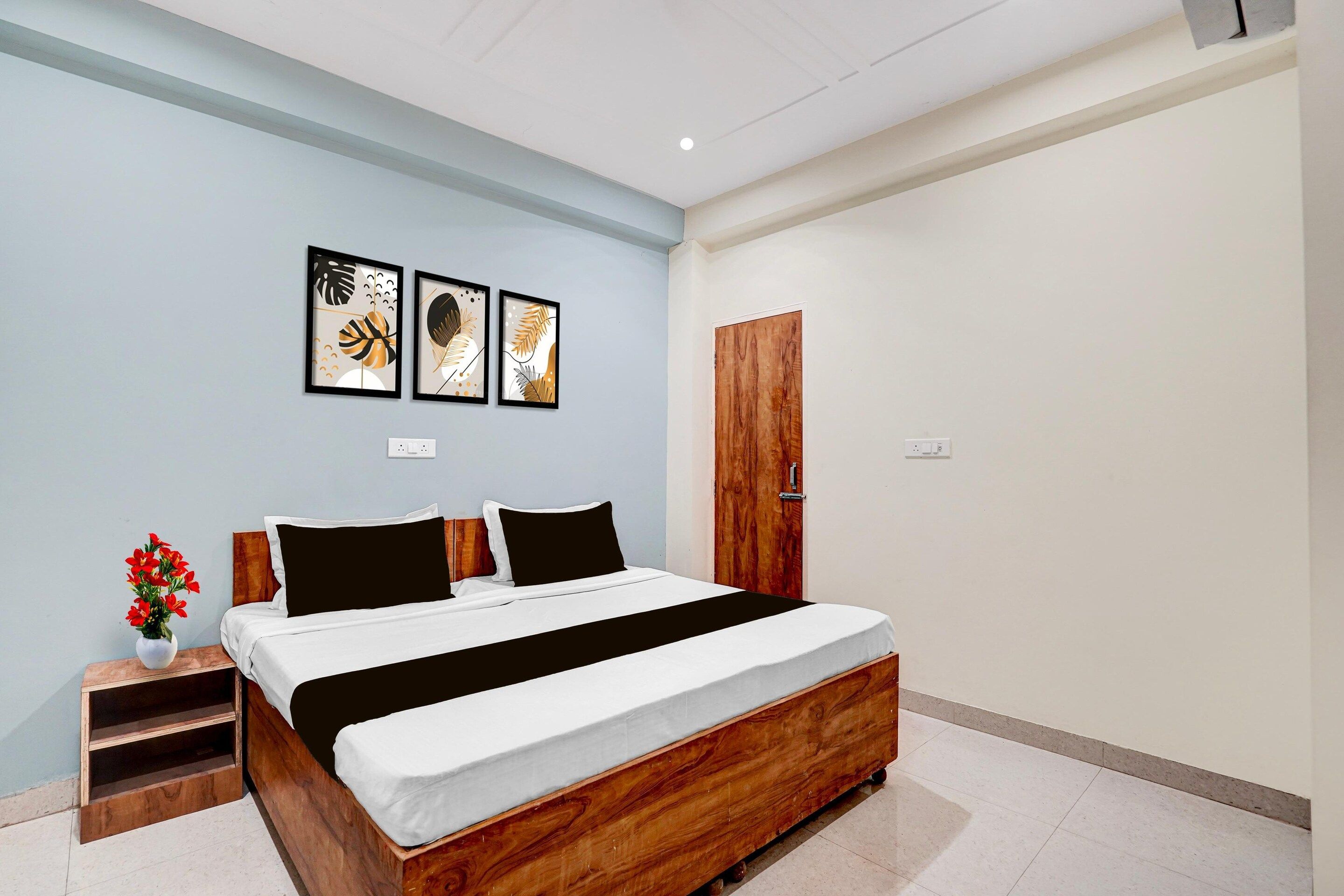 A bedroom with a wooden bed, a nightstand, a vase with flowers, and three framed artworks on the wall.