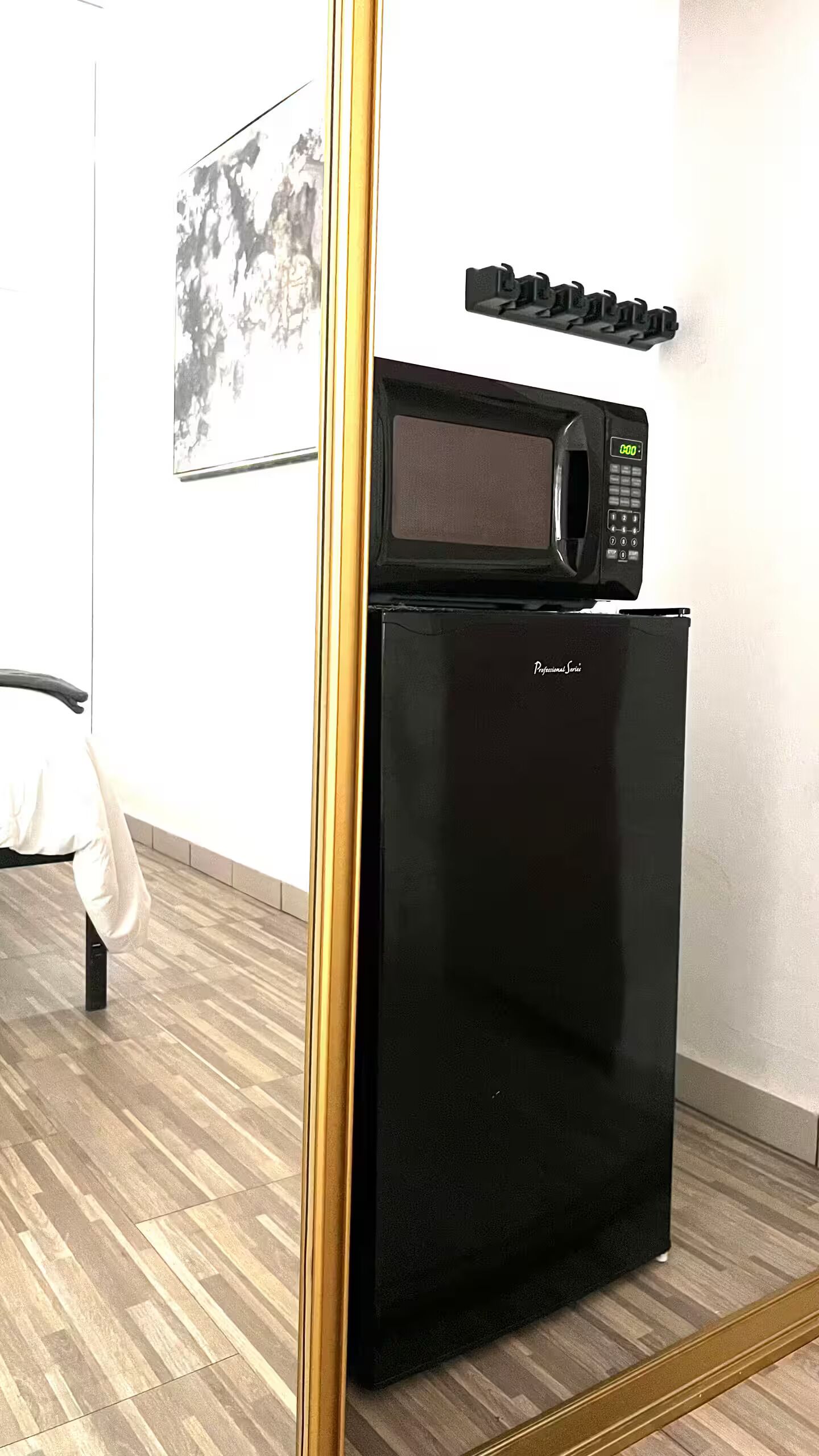 Un réfrigérateur noir avec un micro-ondes posé sur le dessus, une serviette accrochée à une chaise et un tableau encadré au mur.