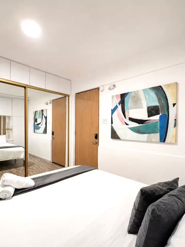 Habitación de hotel con cama, un espejo grande, una puerta de madera y un cuadro en la pared.