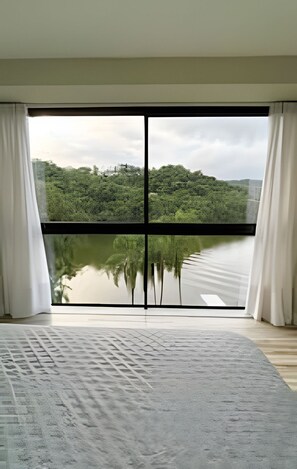 Una habitación con un ventanal grande, una cama y vistas a un lago y un bosque.