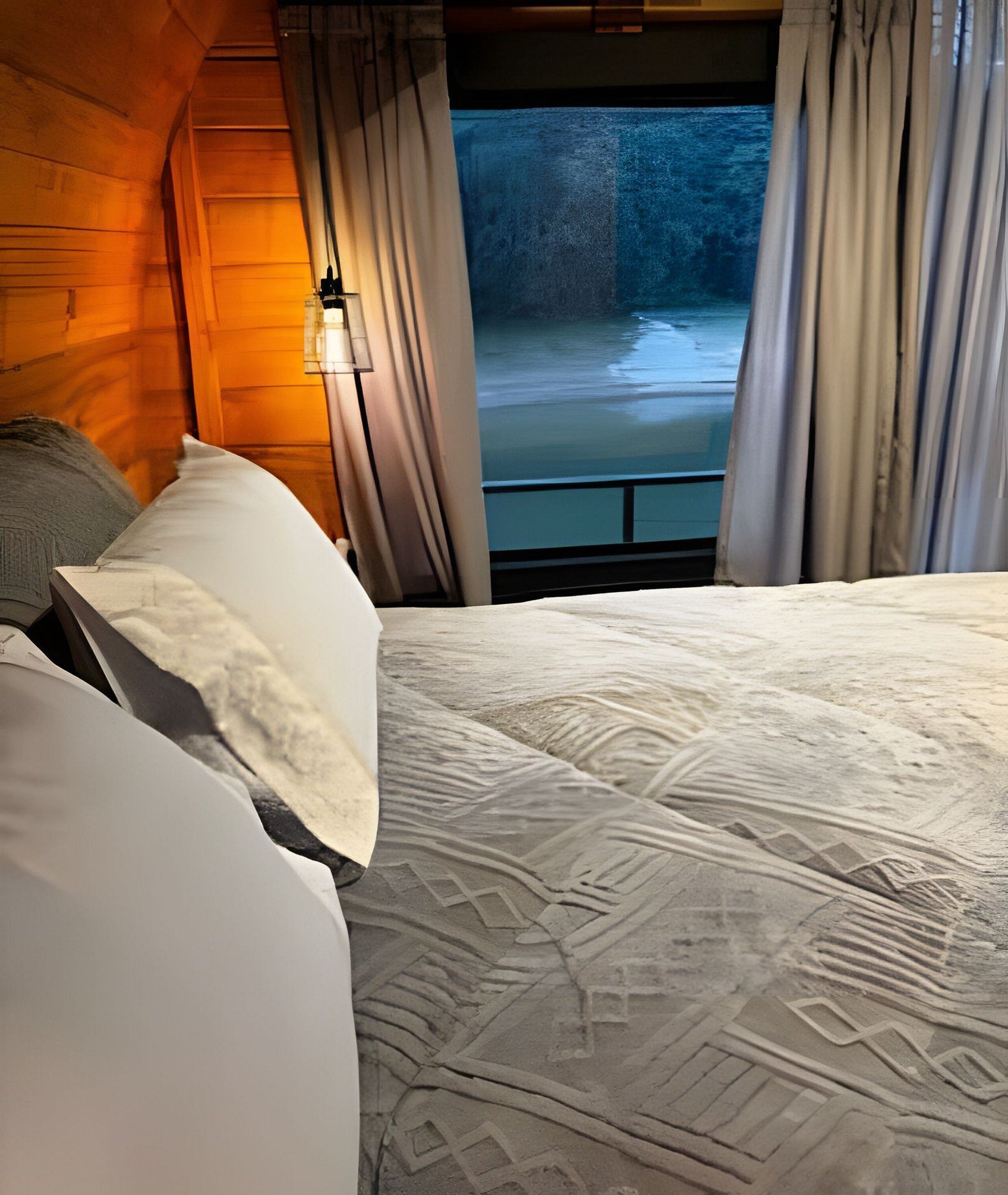Una cama con una colcha estampada, cortinas y vista al río.