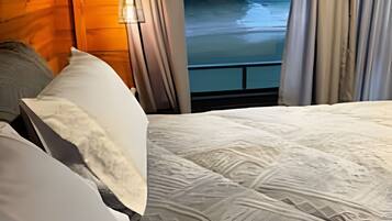 Una cama con una colcha estampada, cortinas y vista al río.