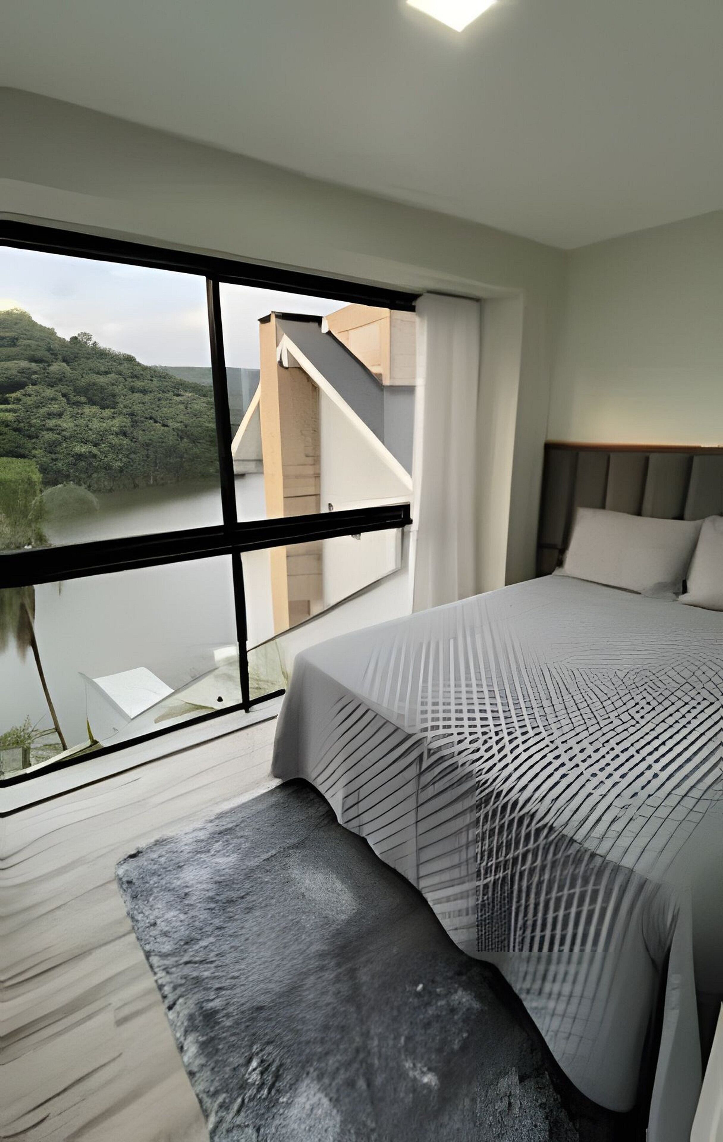 A modern bedroom with a large window, a bed, and a view of a river.