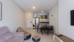 Een moderne woonkamer met een bank, een voetenbankje en een eethoek met stoelen en een tafel.