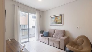 Een woonkamer met een bank, een stoel, een schilderij en uitzicht op een gebouw door een glazen deur.