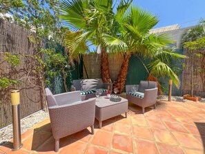Eine möblierte Terrasse im Freien mit Korbmöbeln, einem Tisch mit Flasche und Glas sowie einer Palme.