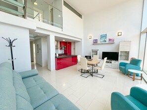A modern living area with a sofa, dining table, chairs, a kitchen with red cabinets, a flat-screen TV, and a balcony with glass railings. - Modern townhouse in Dénia – all-inclusive (Denia)