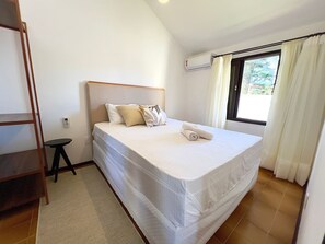 Une chambre à coucher comprenant un lit, une petite table, un climatiseur fixé au mur et une fenêtre avec des rideaux.
