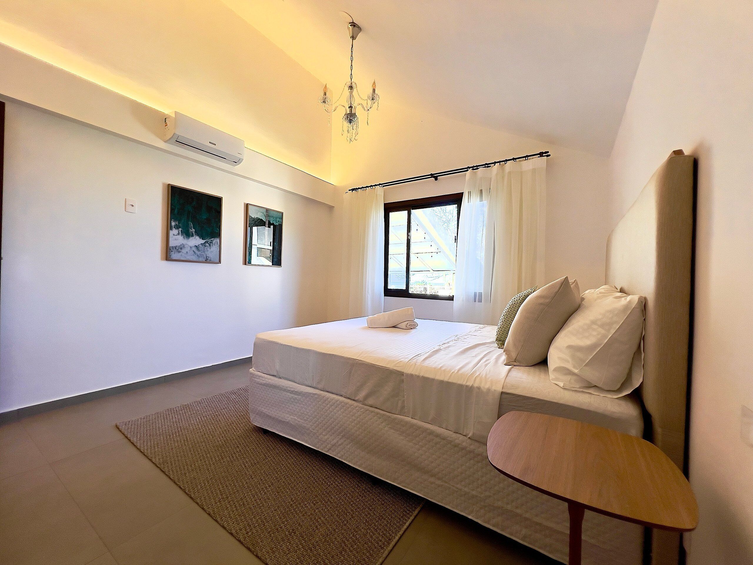 Une chambre à coucher comprenant un lit, une table de chevet, une fenêtre avec des rideaux et des œuvres d’art accrochées au mur.