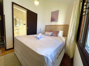 Quarto de hotel com cama, banheiro visível através de uma porta aberta e um quadro na parede.