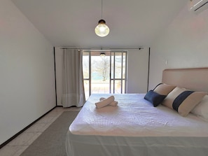 Un dormitorio con cama, cortinas, vistas por un ventanal corredero y una lámpara colgante.