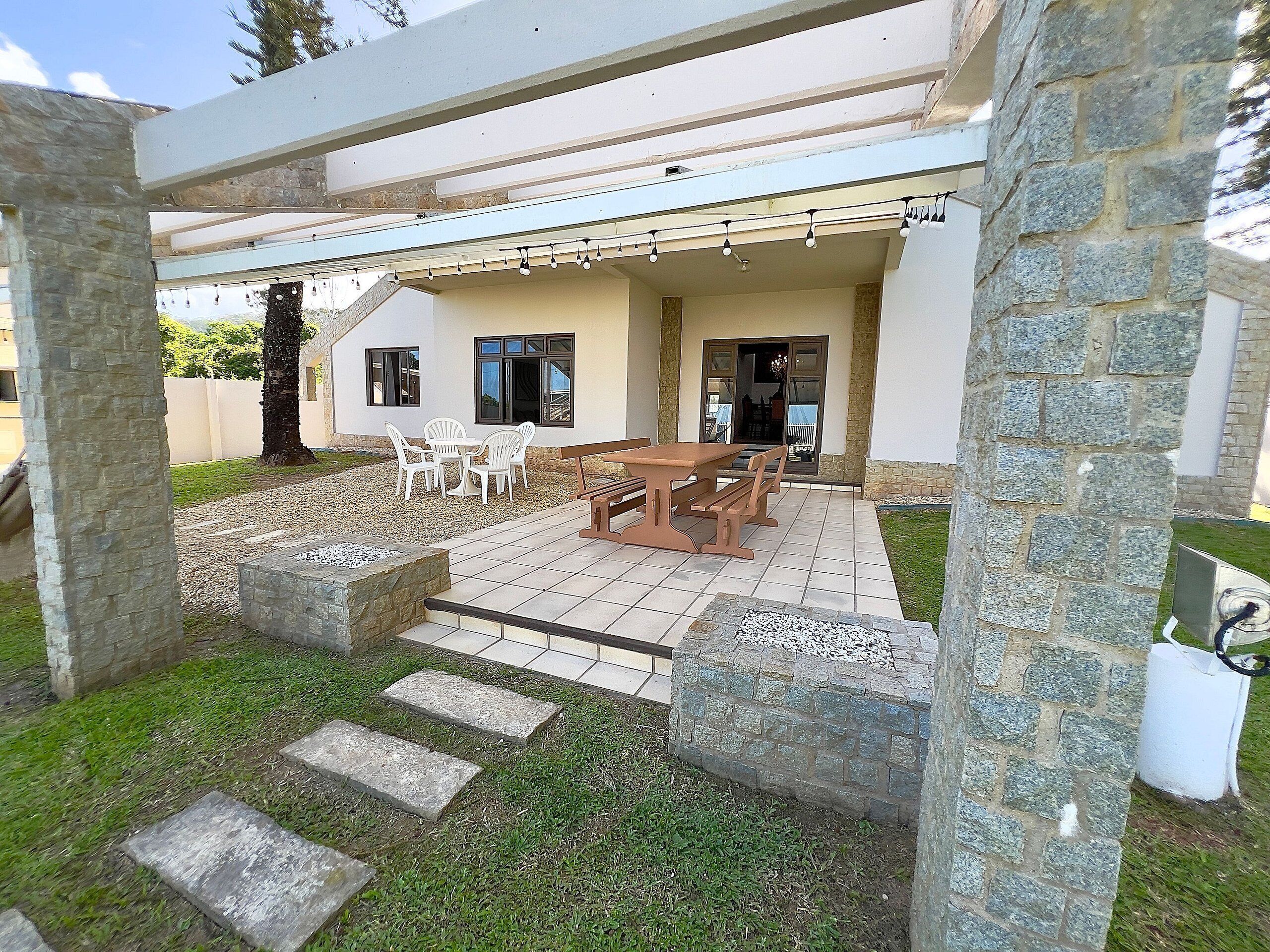 Un patio cubierto con una mesa y sillas, escalones de piedra que llevan a una puerta y una pared de piedra.