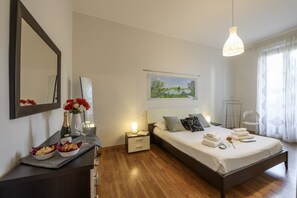 A bedroom with a wooden floor, a bed with pillows and a blanket, a bedside table with a lamp, a nightstand, a mirror, and a painting on the wall. - Lodi, 65 – Your Milan Base (Milan)
