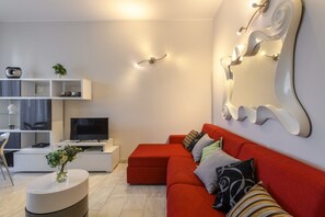 Ein modernes Wohnzimmer mit einem roten Sofa, einem Flachbildfernseher, einer weißen Unterhaltungsecke und einer Wandleuchte.