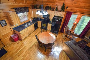 Ein Blockhaushaus-Interieur mit Holzboden, einem Esstisch, Stühlen, einer Küchenzeile inklusive Kühlschrank, Herd und Spüle.