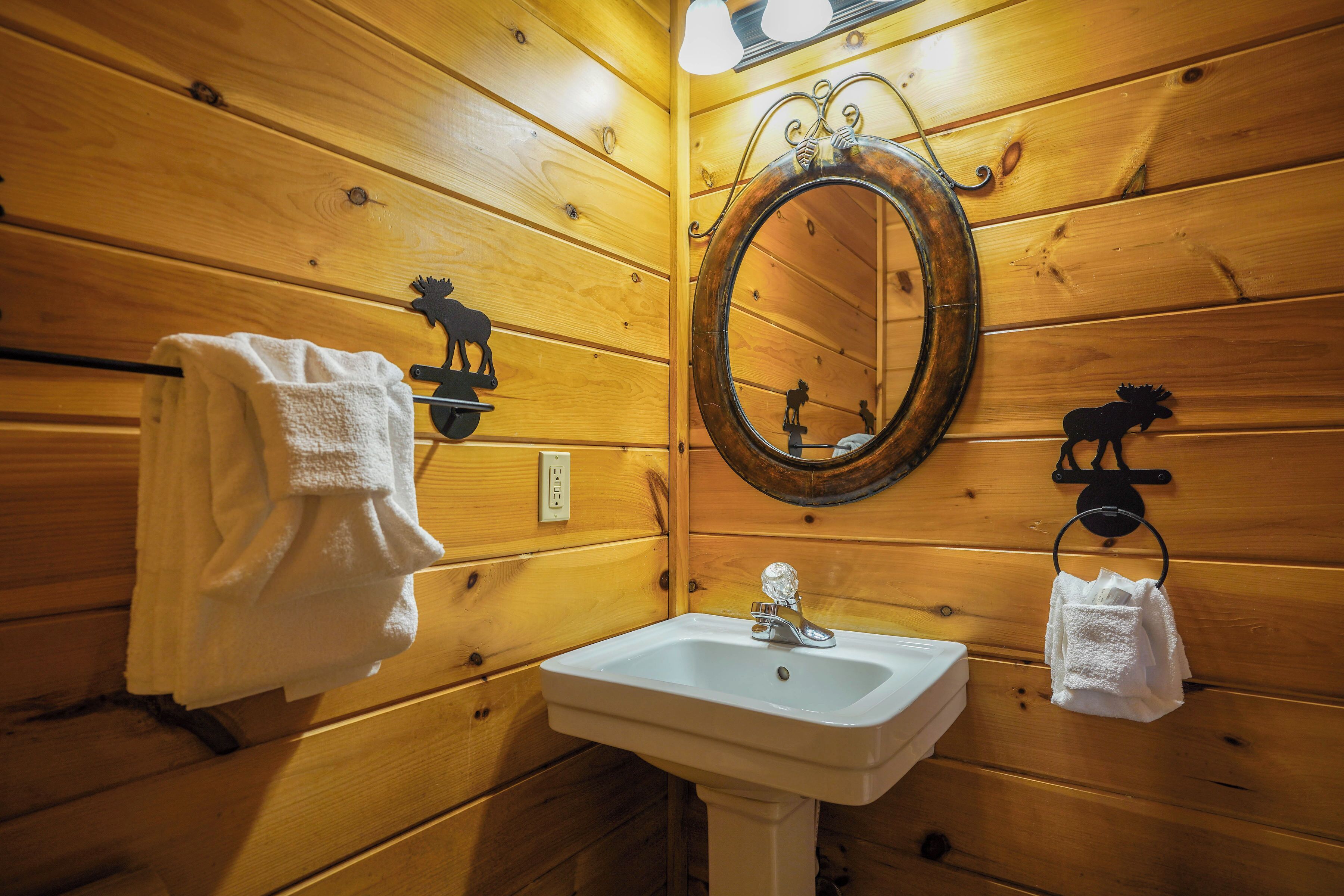 Ein Badezimmer mit Holzwandverkleidung, einem weißen Waschbecken, einem Spiegel und zwei Handtuchhaltern.