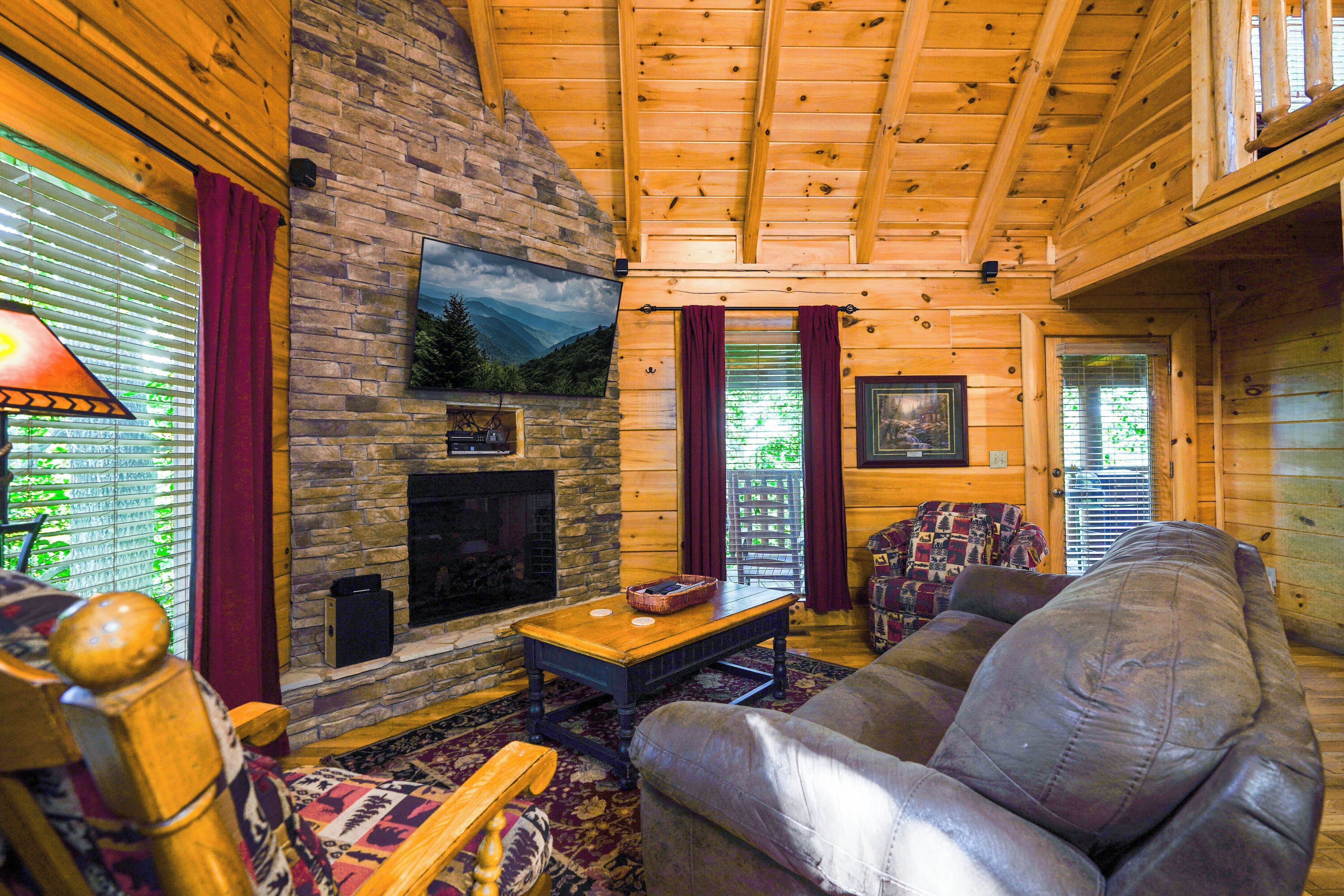 A cozy cabin interior with a stone fireplace, wooden walls, and a comfortable seating area.