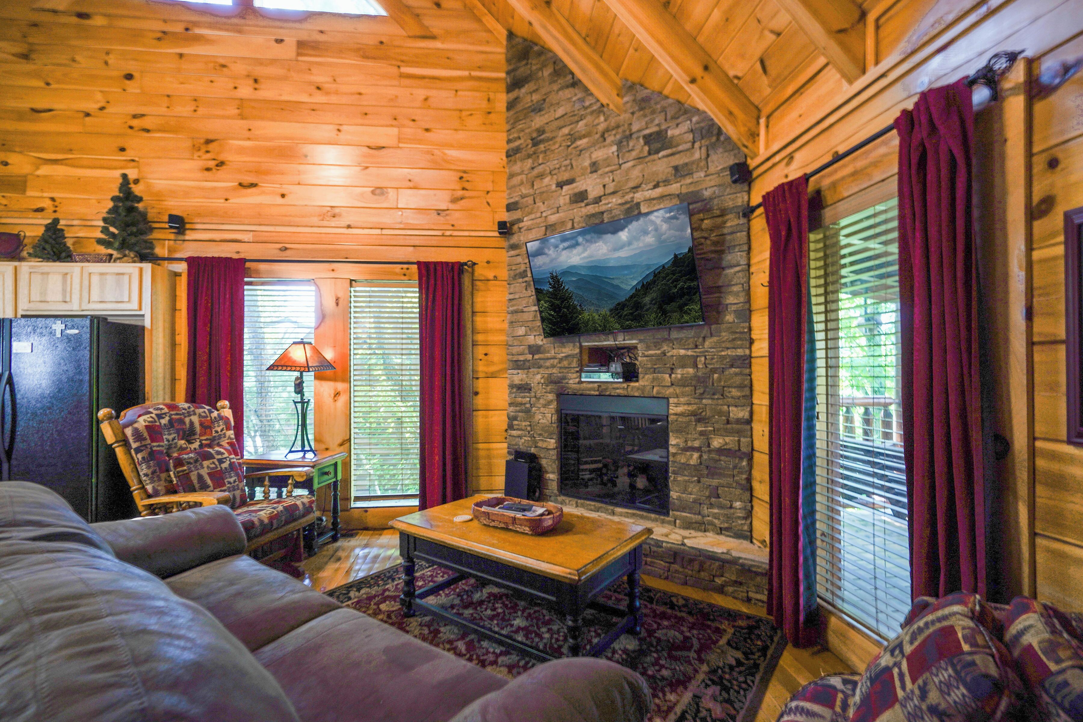 A cozy living room with a stone fireplace, wooden ceiling, and a television mounted above it.