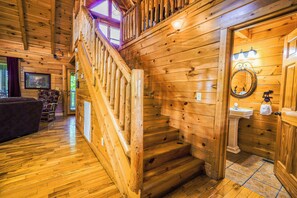 A wooden interior with a staircase, a living area with a couch, and a bathroom with a sink and mirror.